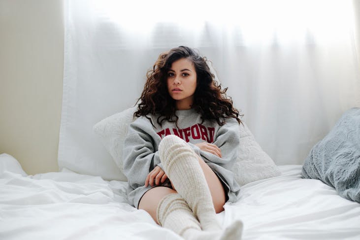 A girl sitting on a bed with white sheets.